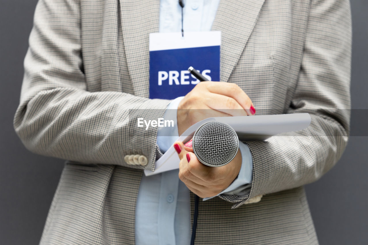 Female reporter at news conference or media event, writing notes, holding microphone