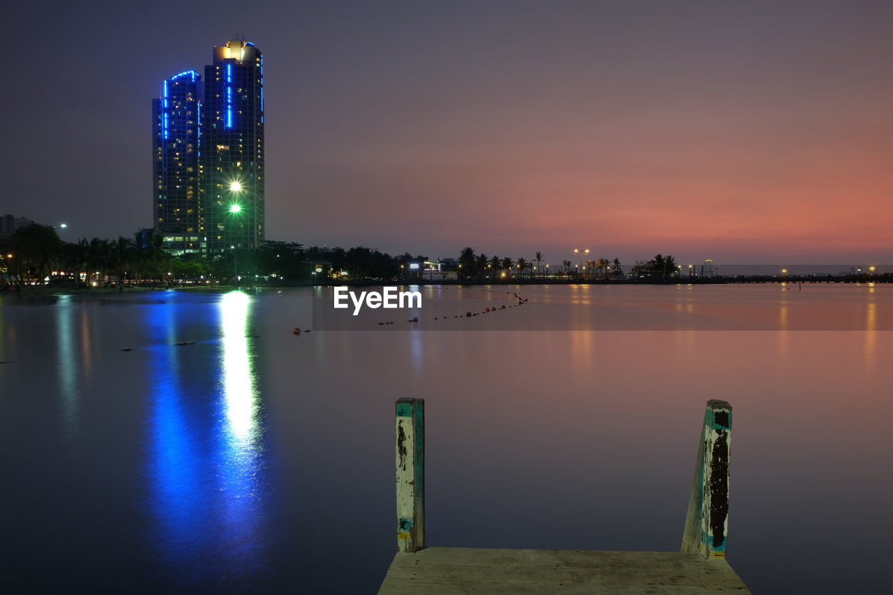 Scenic view of lake by illuminated buildings against sky at night