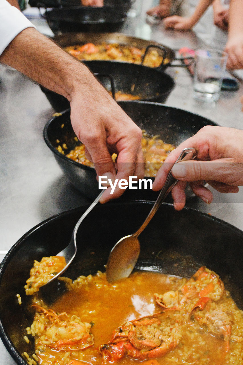 Close-up of men hands tasting food in cooking pans. 