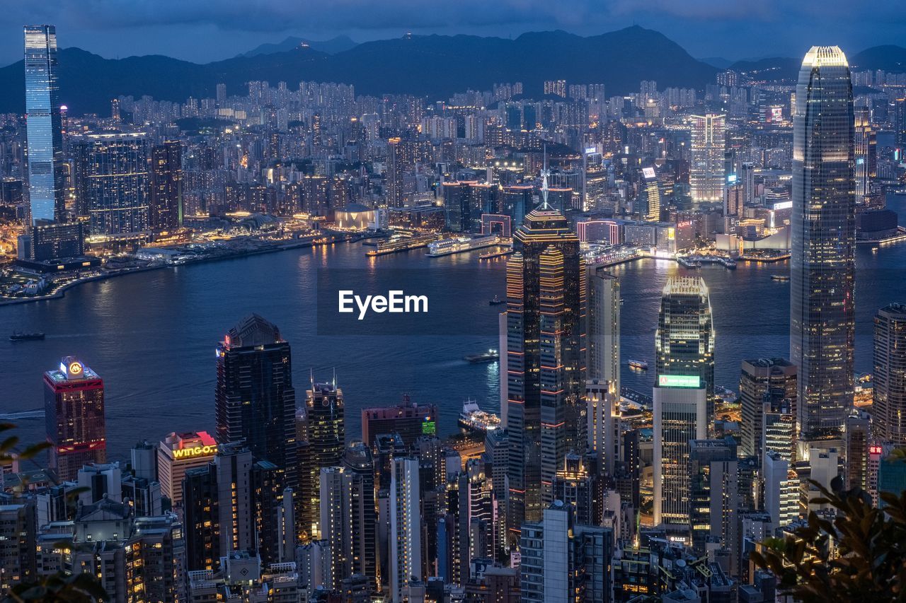 HIGH ANGLE VIEW OF ILLUMINATED CITY BY SEA AND BUILDINGS