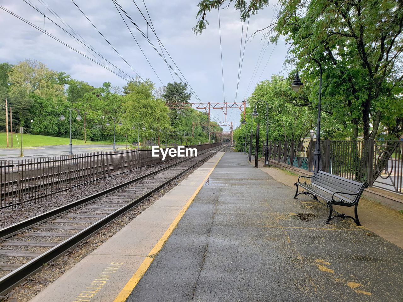 Empty railroad tracks by trees against sky