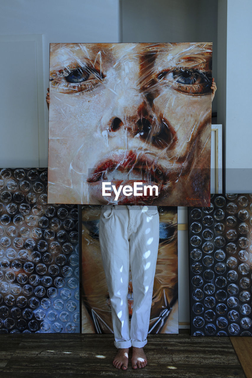 Female artist standing behind painting against wall in art studio