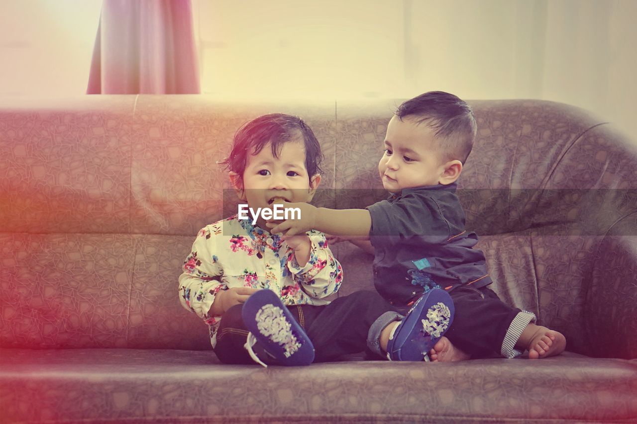 Cute siblings sitting on sofa at home