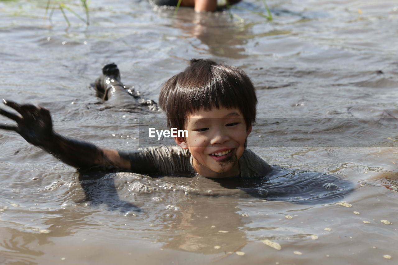 Messy boy smiling while lying in muddy water