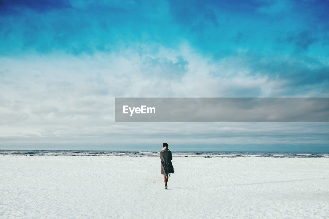 Woman standing at baltic seashore against cloudy sky during winter