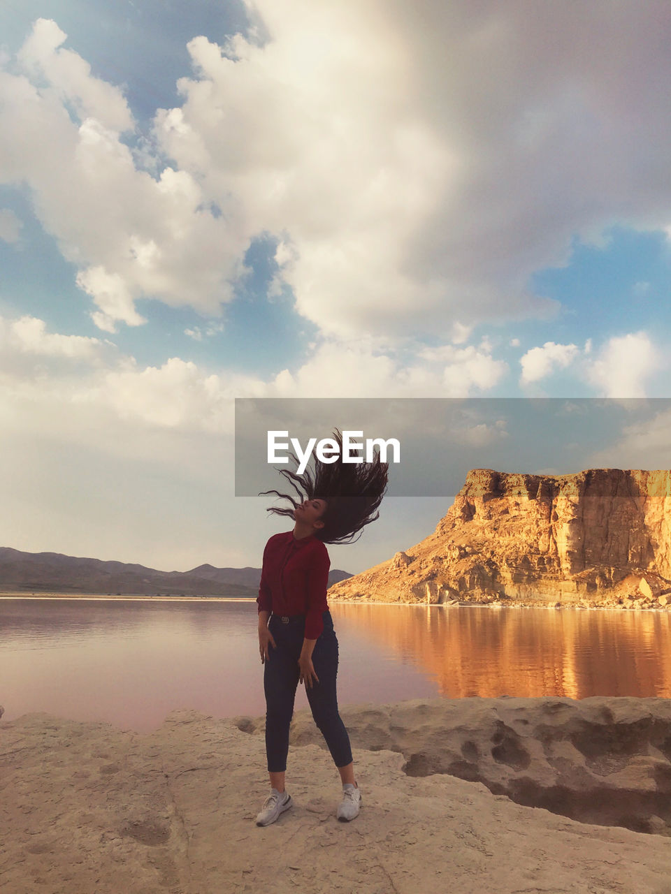 REAR VIEW OF WOMAN STANDING ON SHORE AGAINST SKY