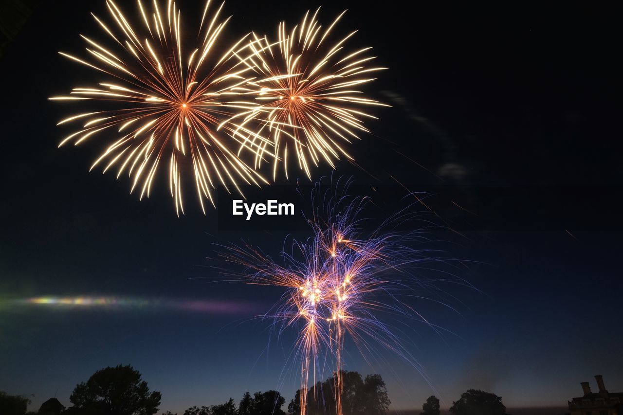 Low angle view of firework display over river against sky