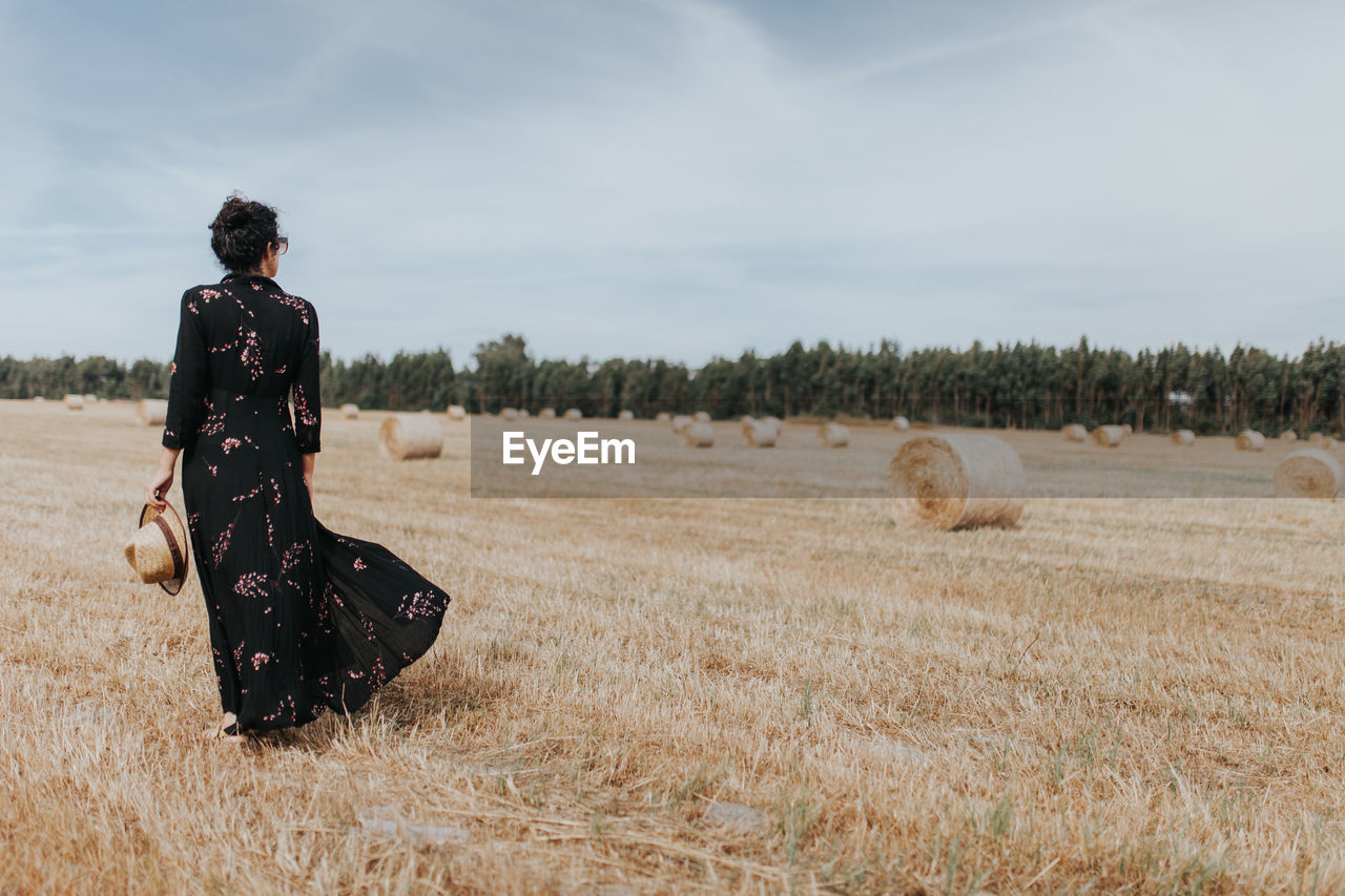 Rear view of woman by hay bales on field