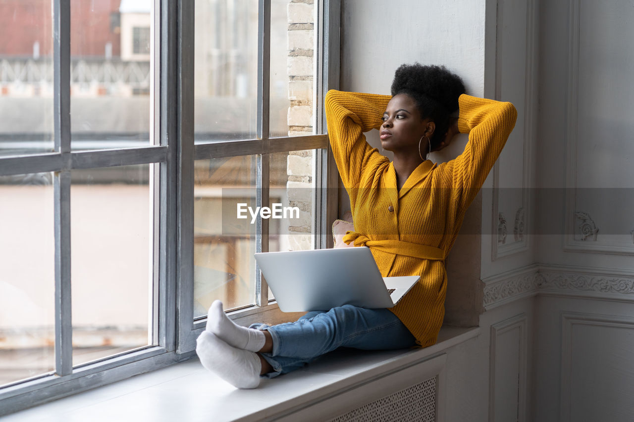 Young woman with laptop sitting by window at home