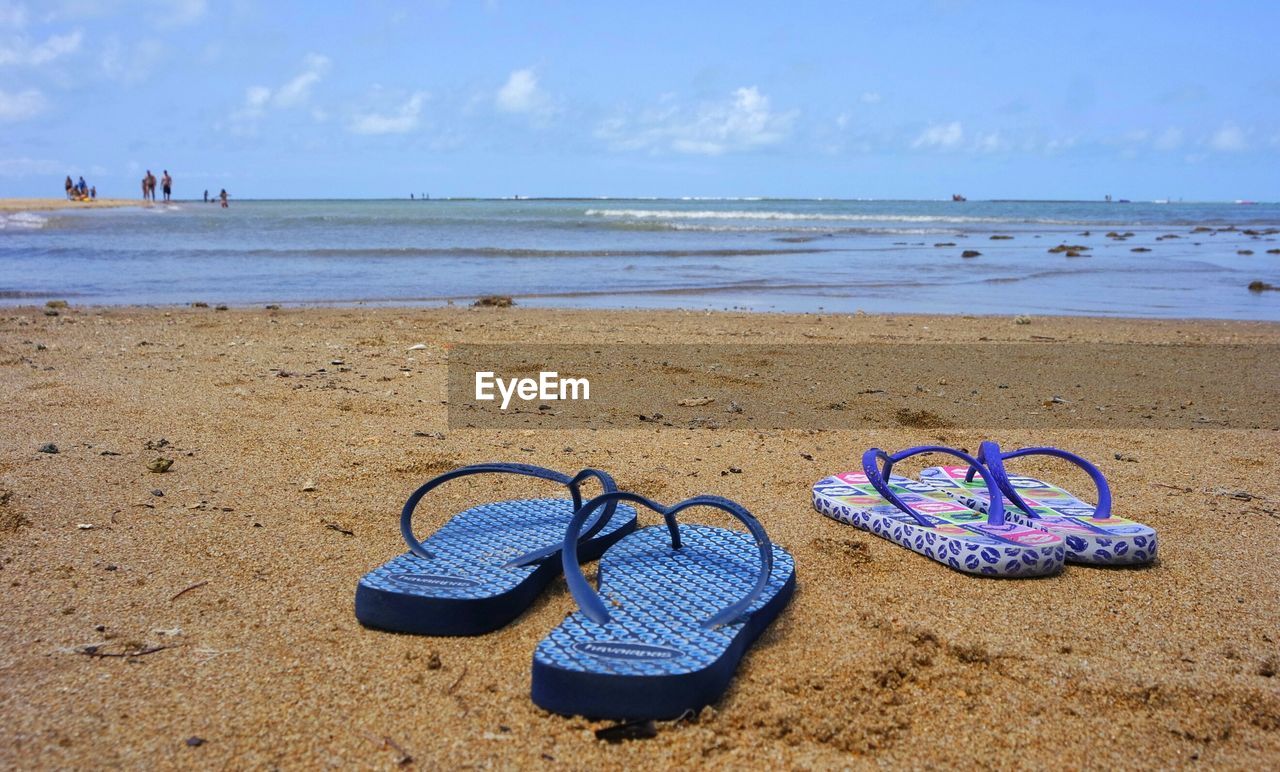 Slippers at beach against sky on sunny day