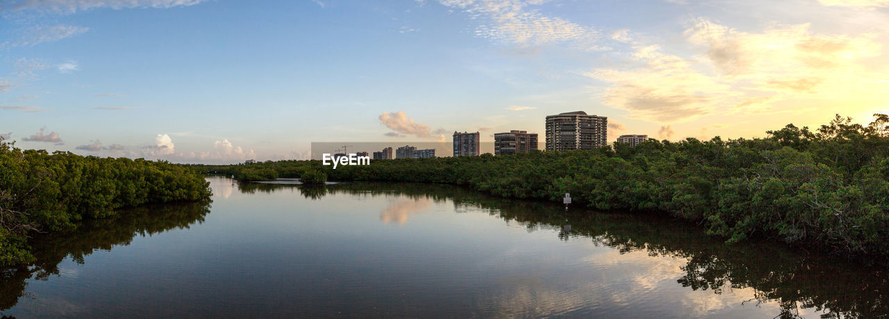 Scenic view of river by buildings against sky during sunset