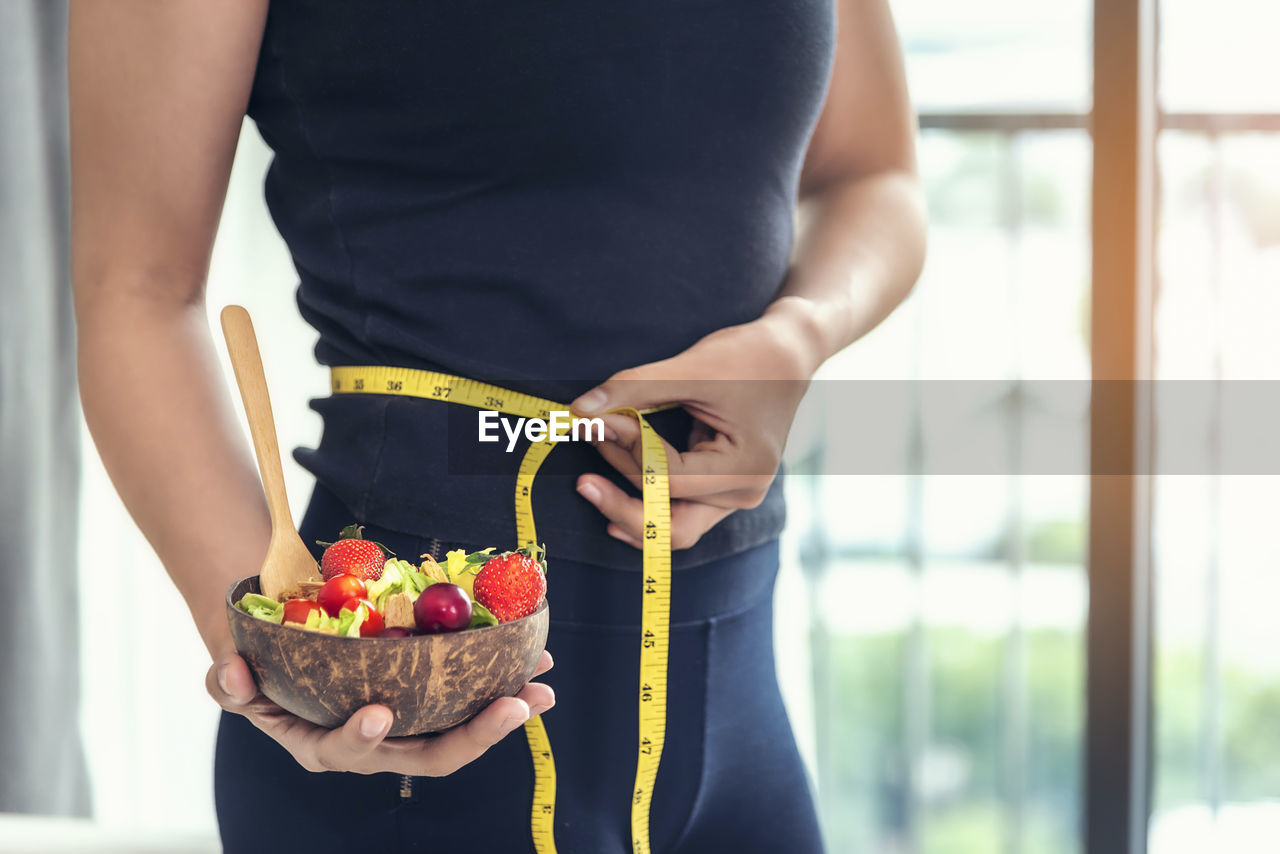 Midsection of woman measuring waist at home