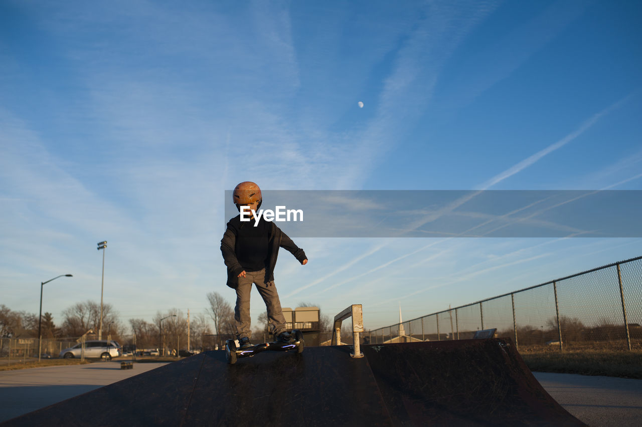 Young boy in helmet riding down pyramid ramp at skate park