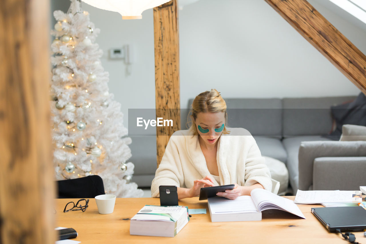 Businesswoman using digital tablet at home by christmas tree