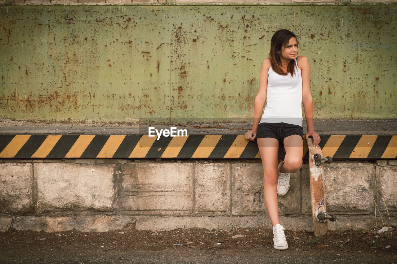 Young woman looking away while standing against wall