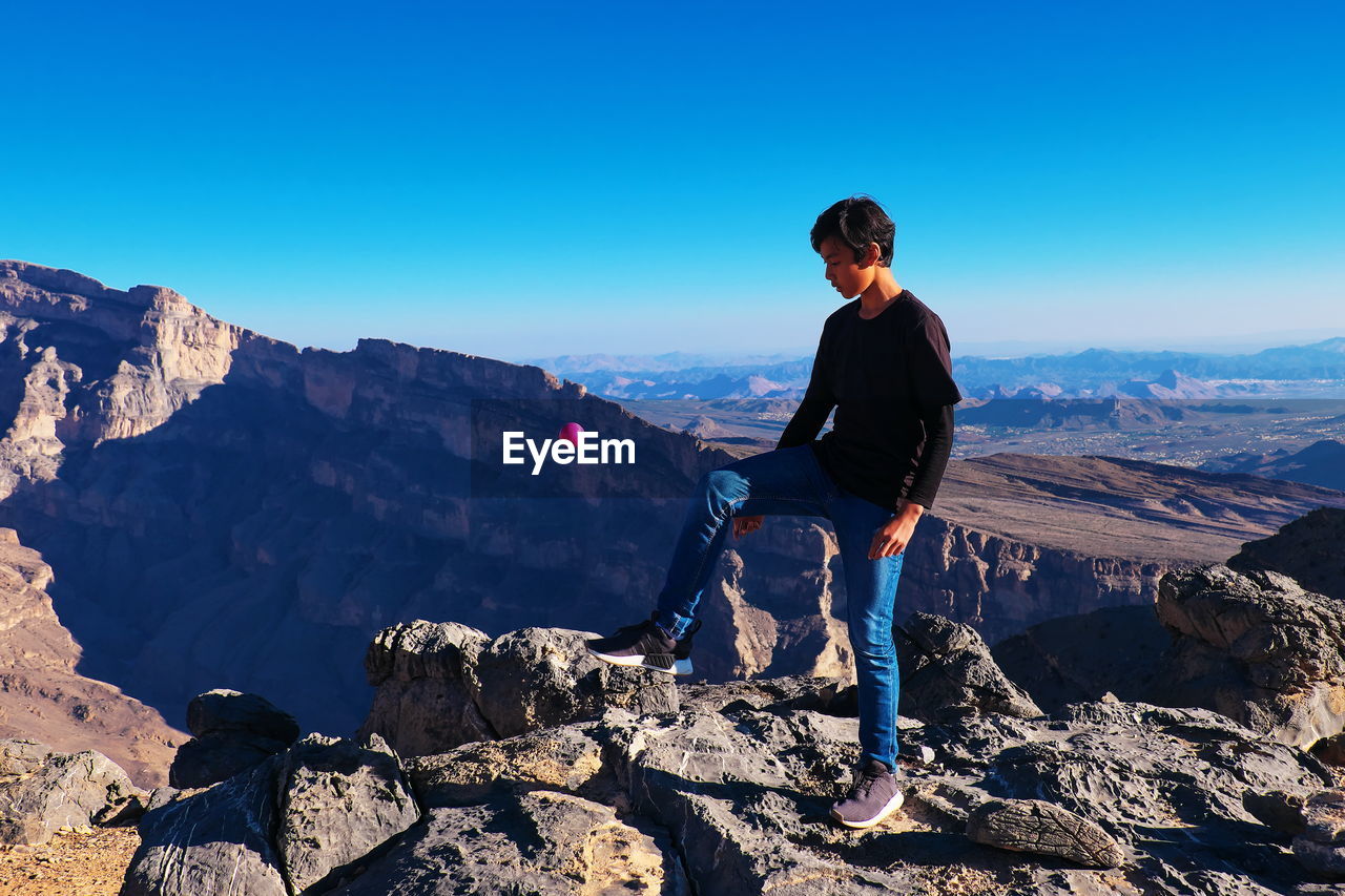 Full length of teenage boy standing on mountain against sky