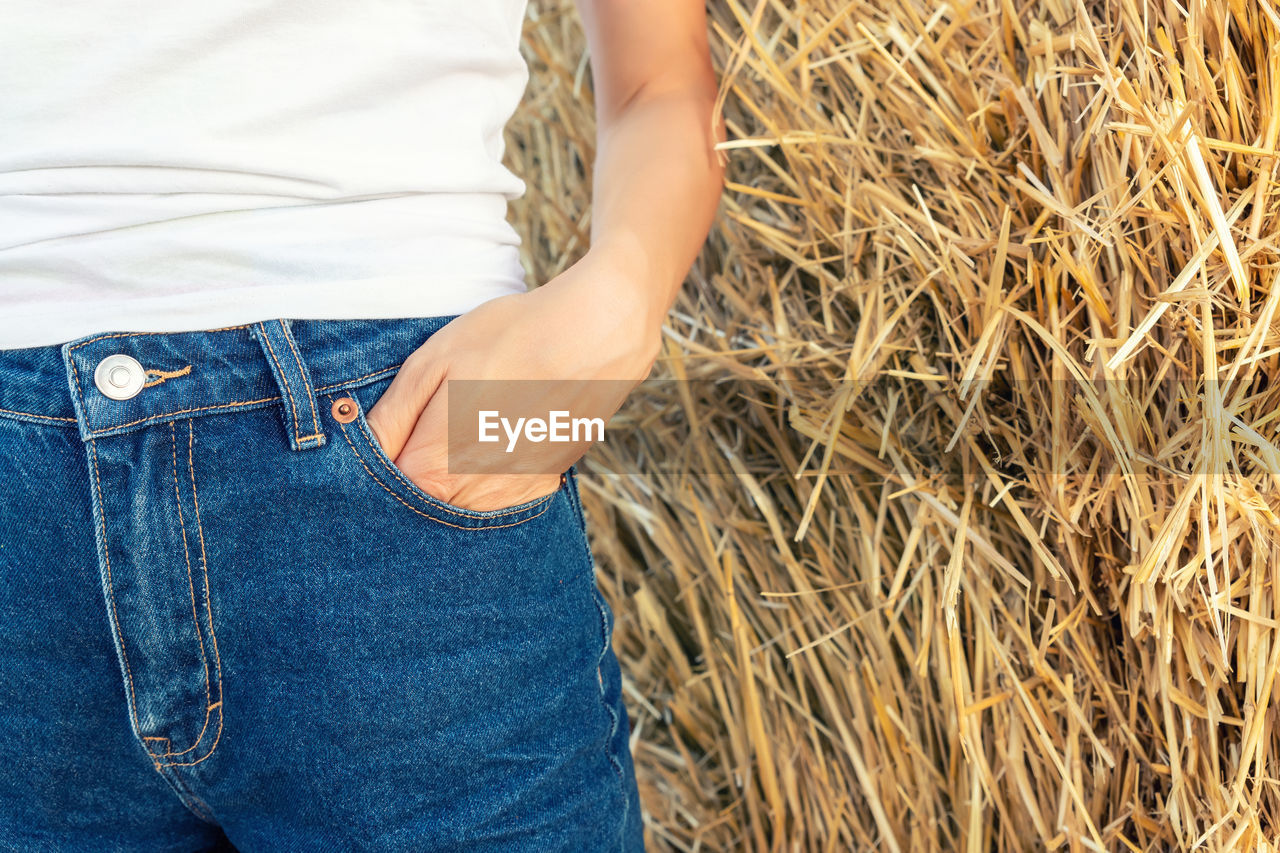 Midsection of woman with hand in pocket against hay bale