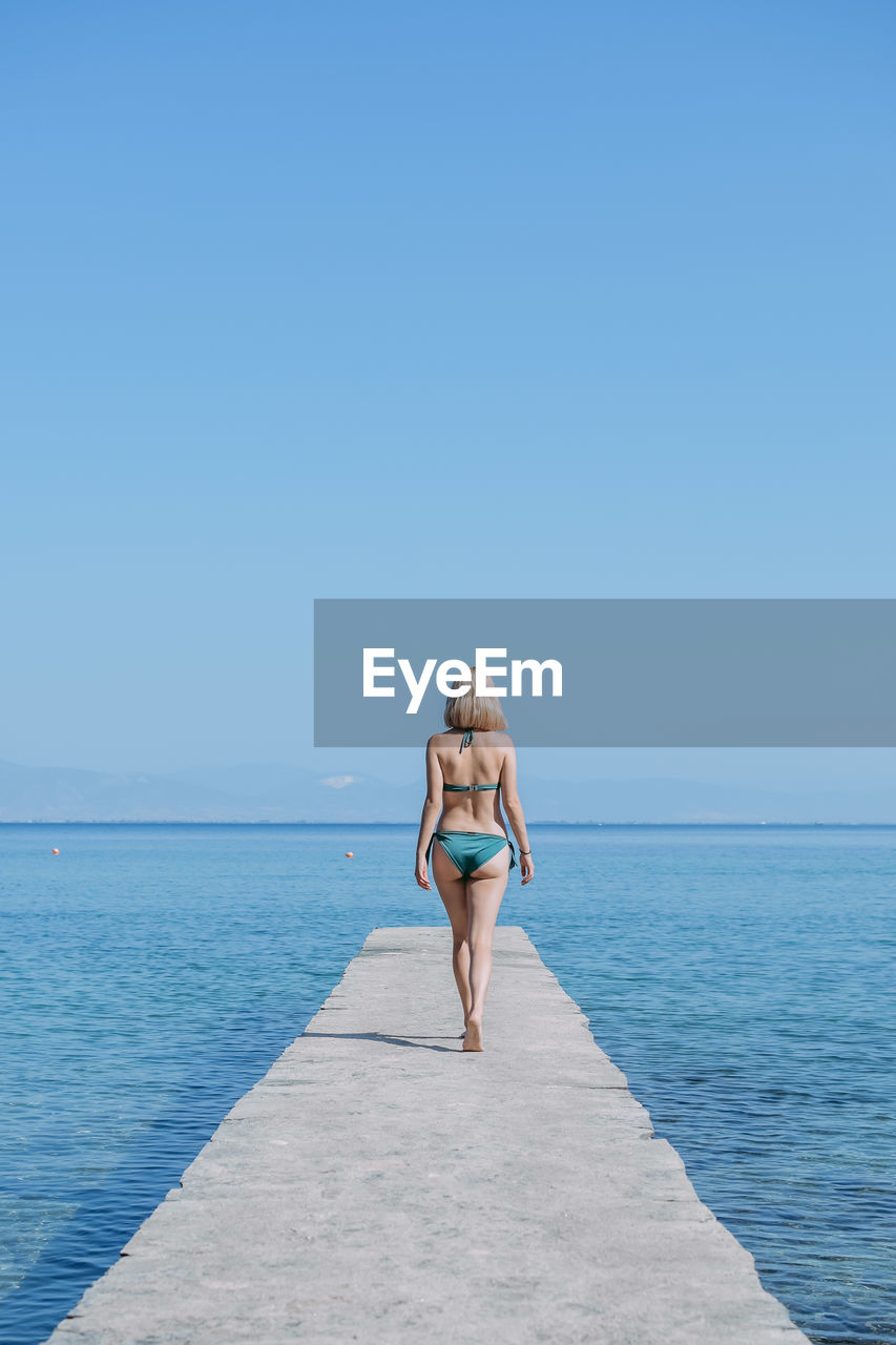 MAN STANDING ON SEA AGAINST CLEAR SKY