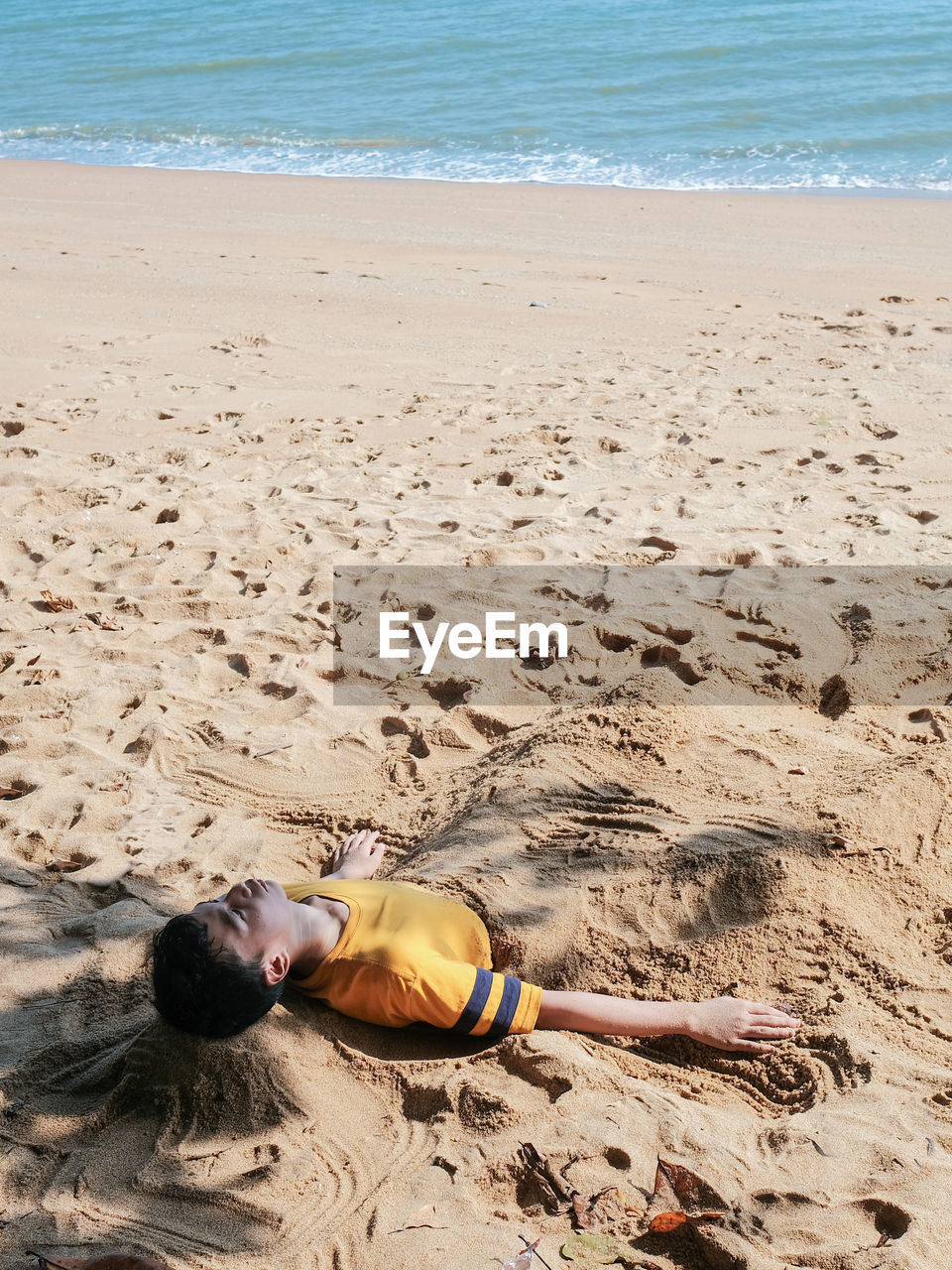 High level view of a boy burying himself with sand on the beach