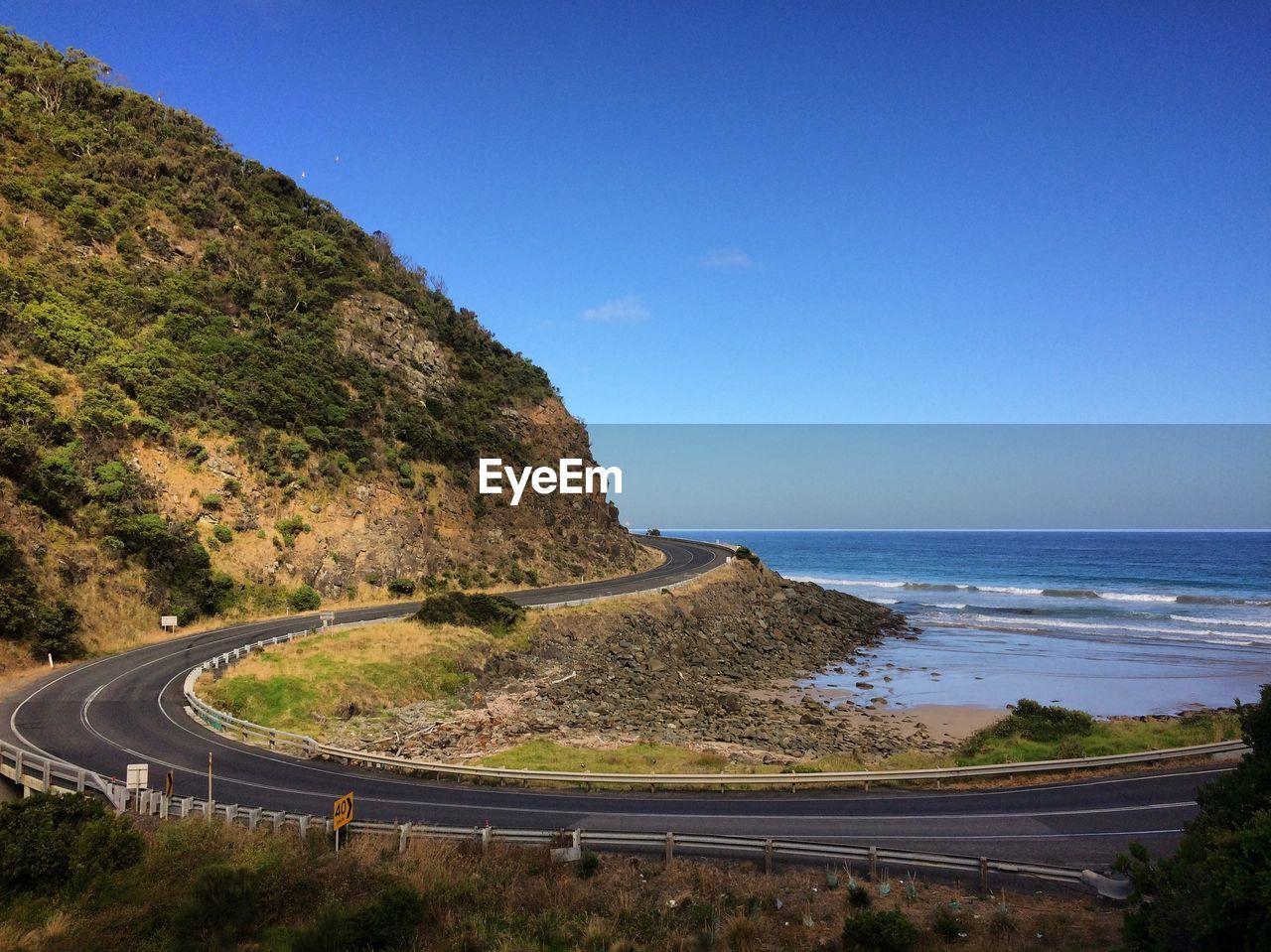 Scenic view of road by sea against clear blue sky