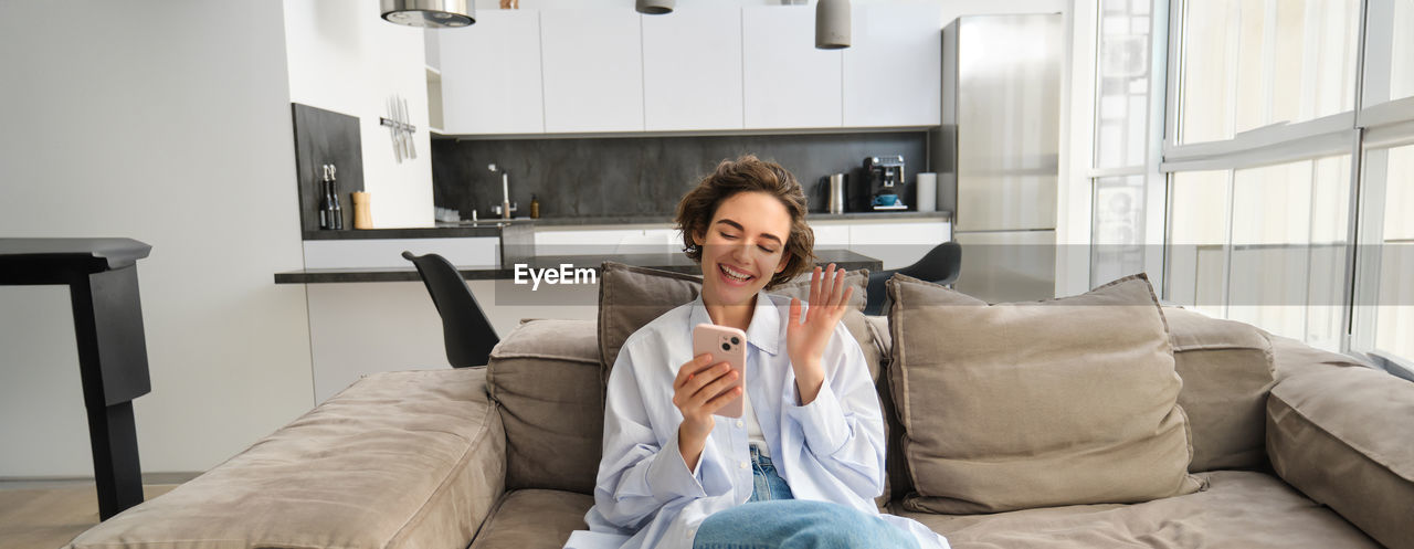 portrait of young woman using mobile phone while sitting at home