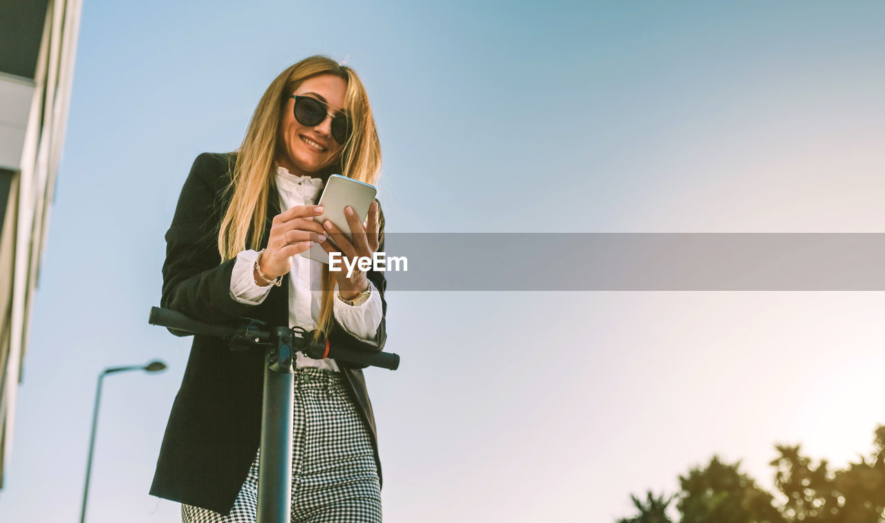 YOUNG WOMAN WEARING SUNGLASSES STANDING AGAINST SKY