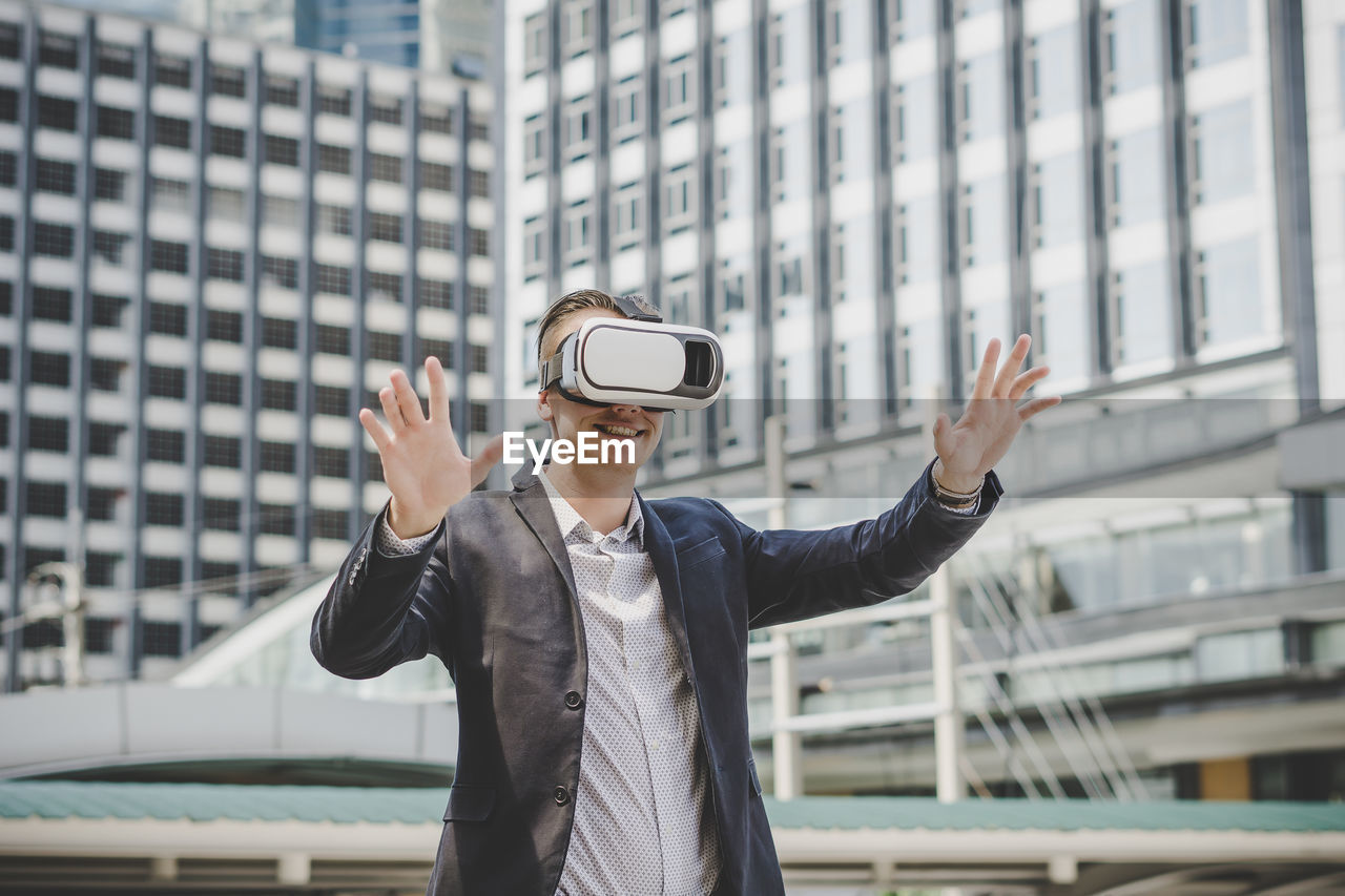 Businessman looking through virtual reality simulator while standing against building