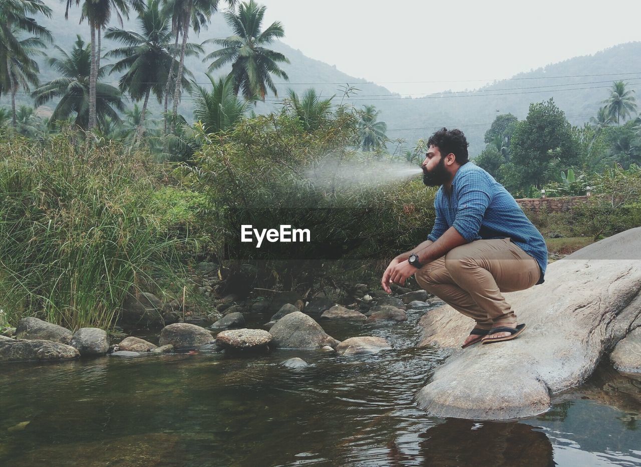 Man spraying water from mouth by river