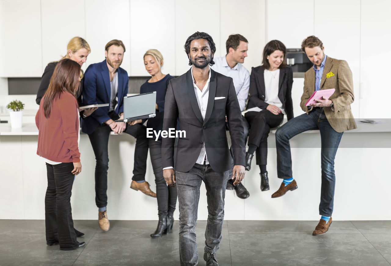 Portrait of mid adult businessman standing with colleagues discussing in background at office