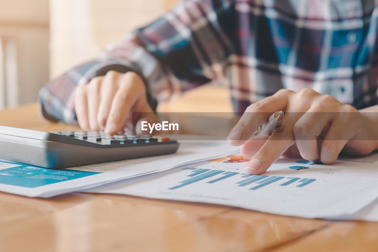 Midsection of woman analyzing chart with calculator on office desk