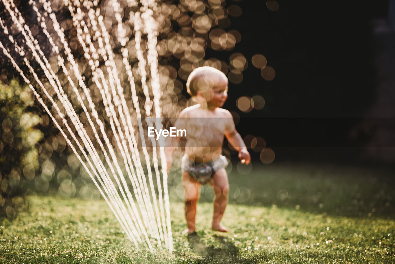 Bokeh baby in garden playing with water from sprinkler