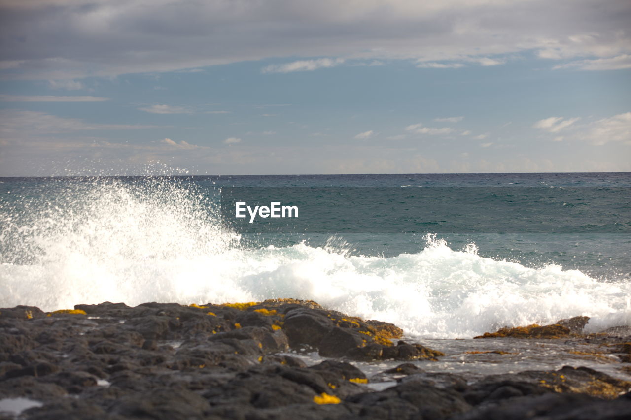 Waves splashing on rocks at shore against sky