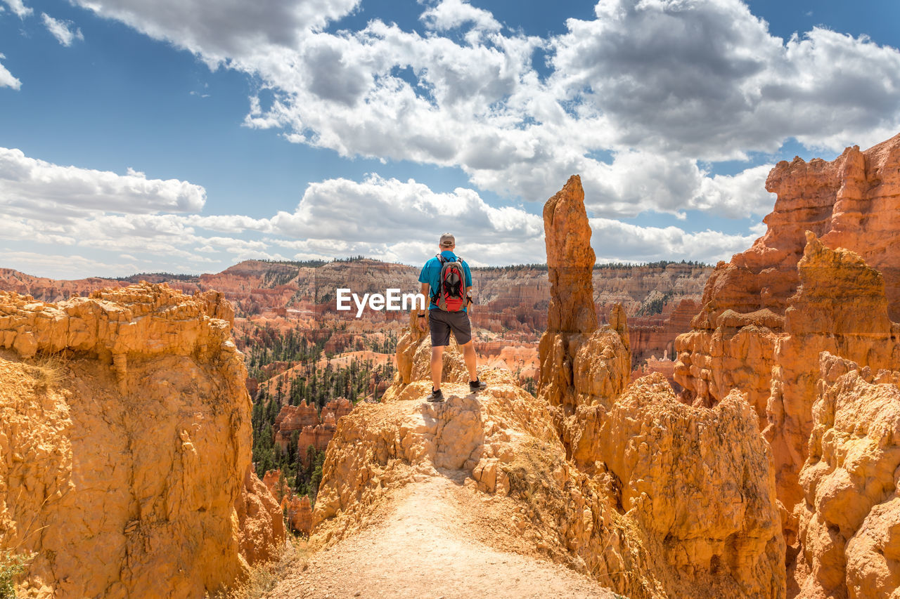 Rear view of man standing on rock formation against sky