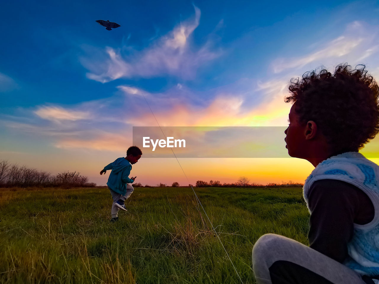 BOY ON FIELD AGAINST SKY DURING SUNSET