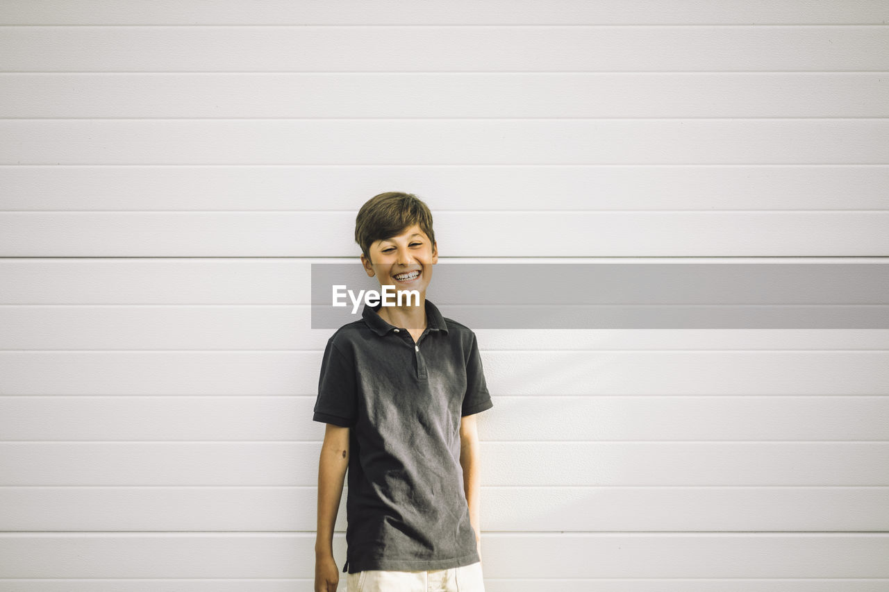 Portrait of happy boy standing against white wall