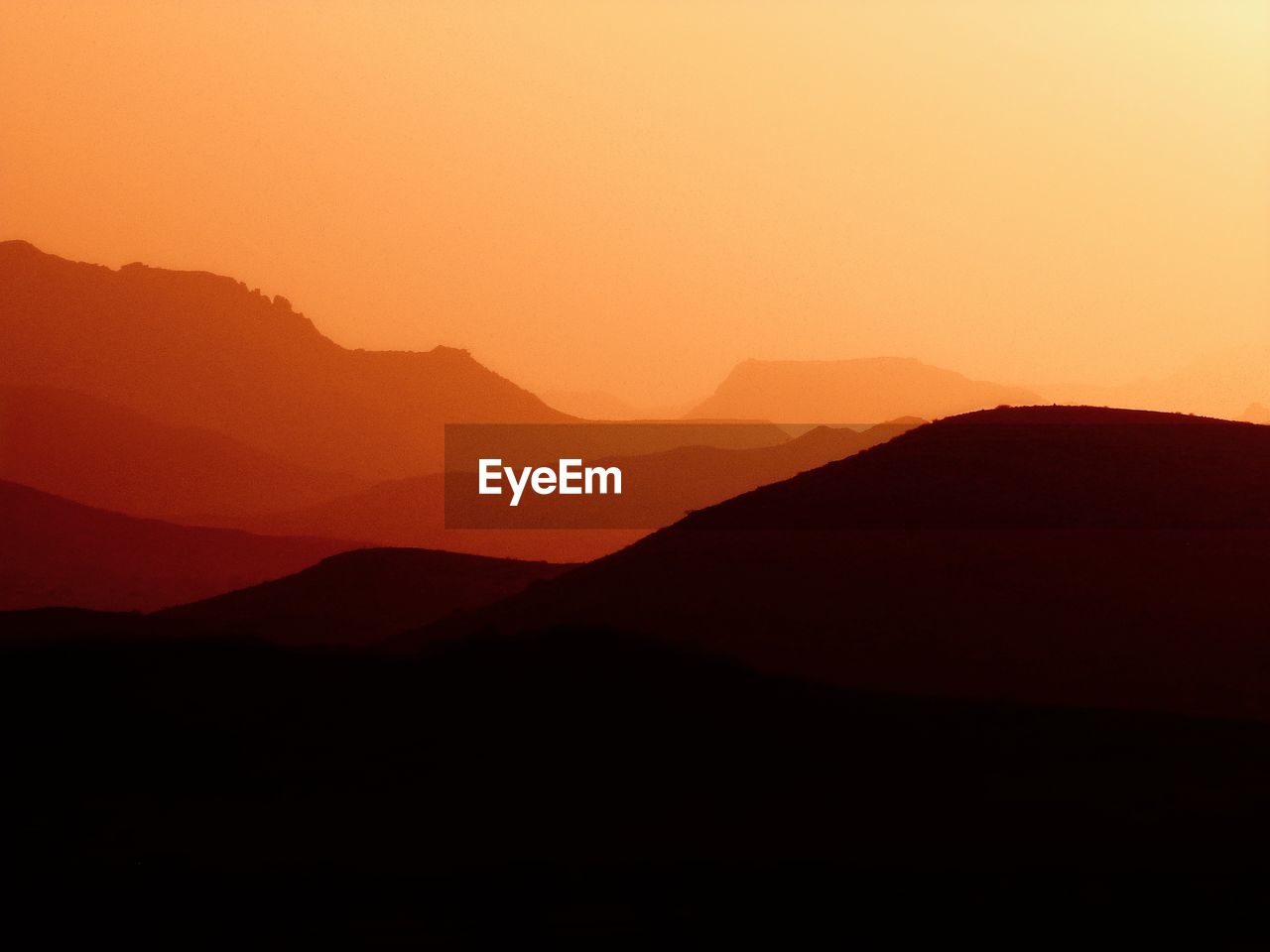 Scenic view of silhouette mountains against orange sky