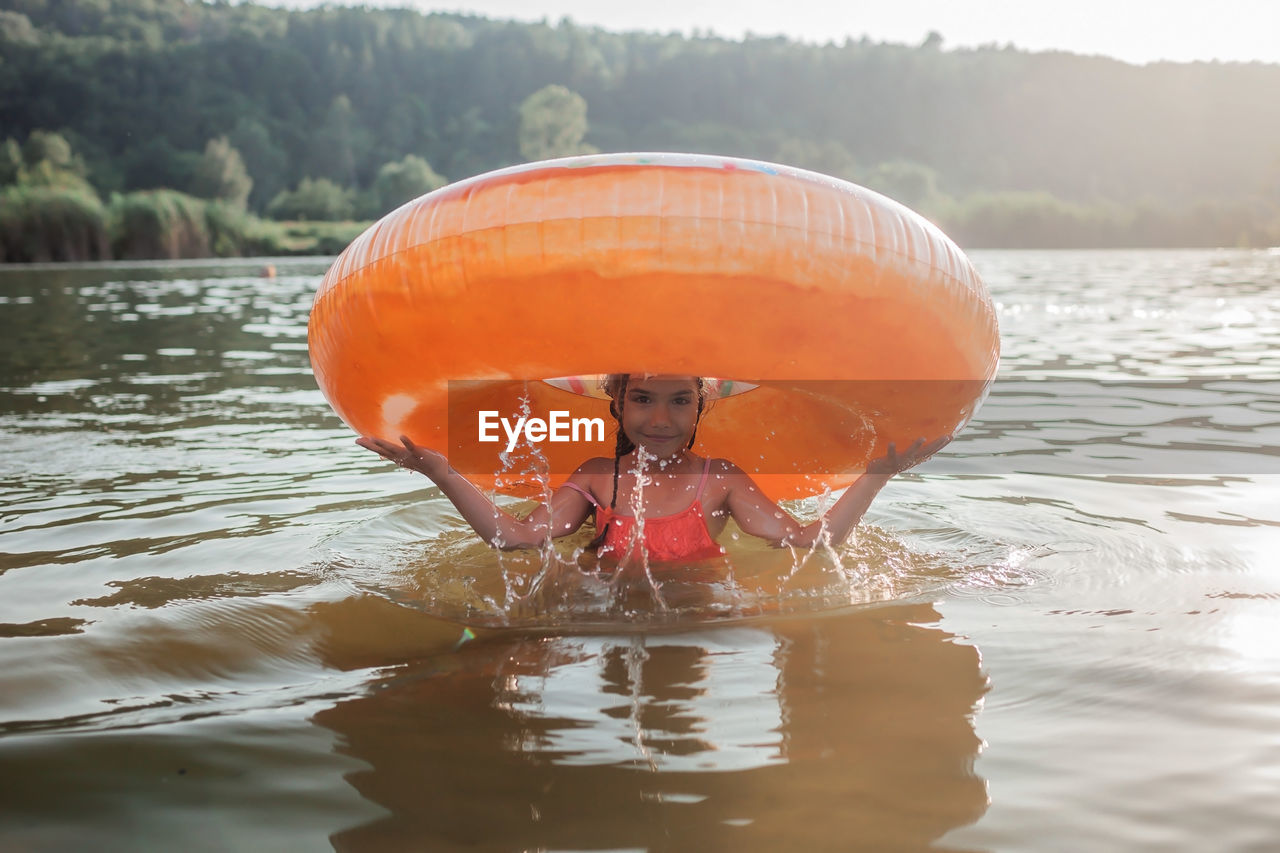 Girl has fun on big donut inflatable ring on lake on hot summer day, happy summertime, countryside