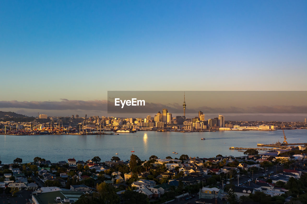 Illuminated cityscape by sea against sky during sunset