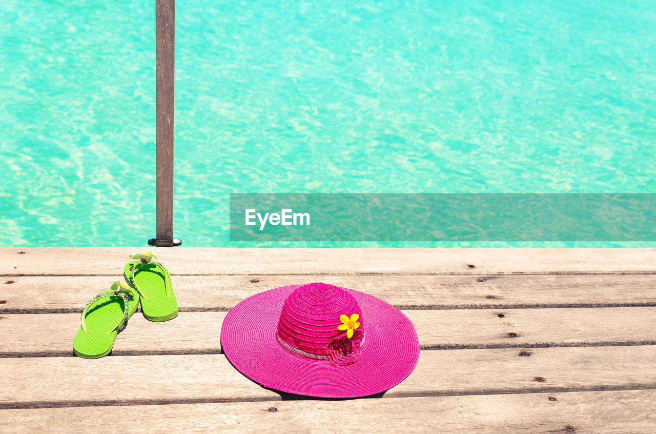 High angle view of flip-flop with sun hat on wooden table by swimming pool