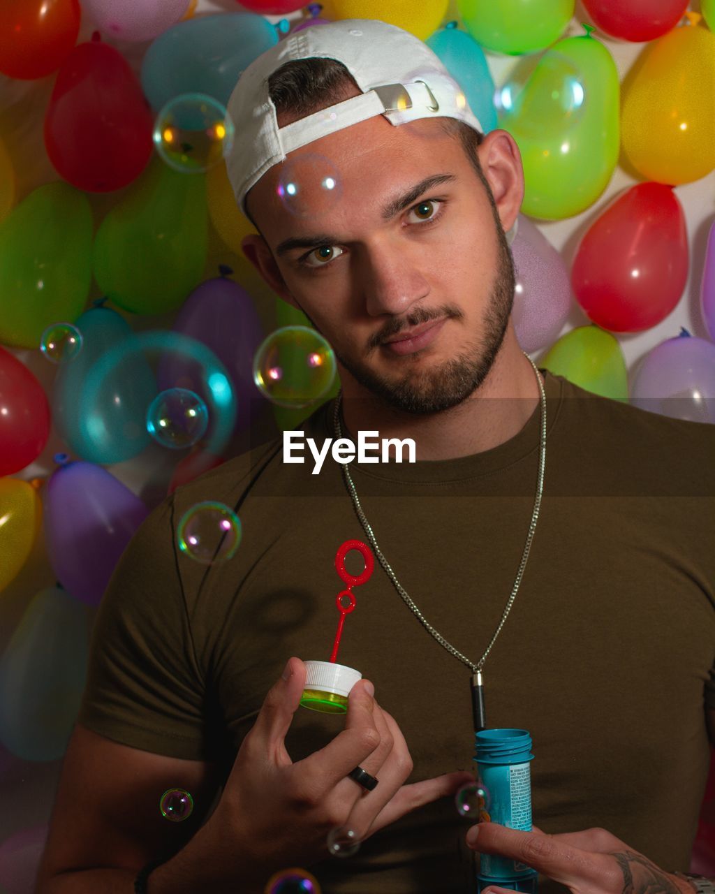 Portrait of young man blowing bubbles against balloons