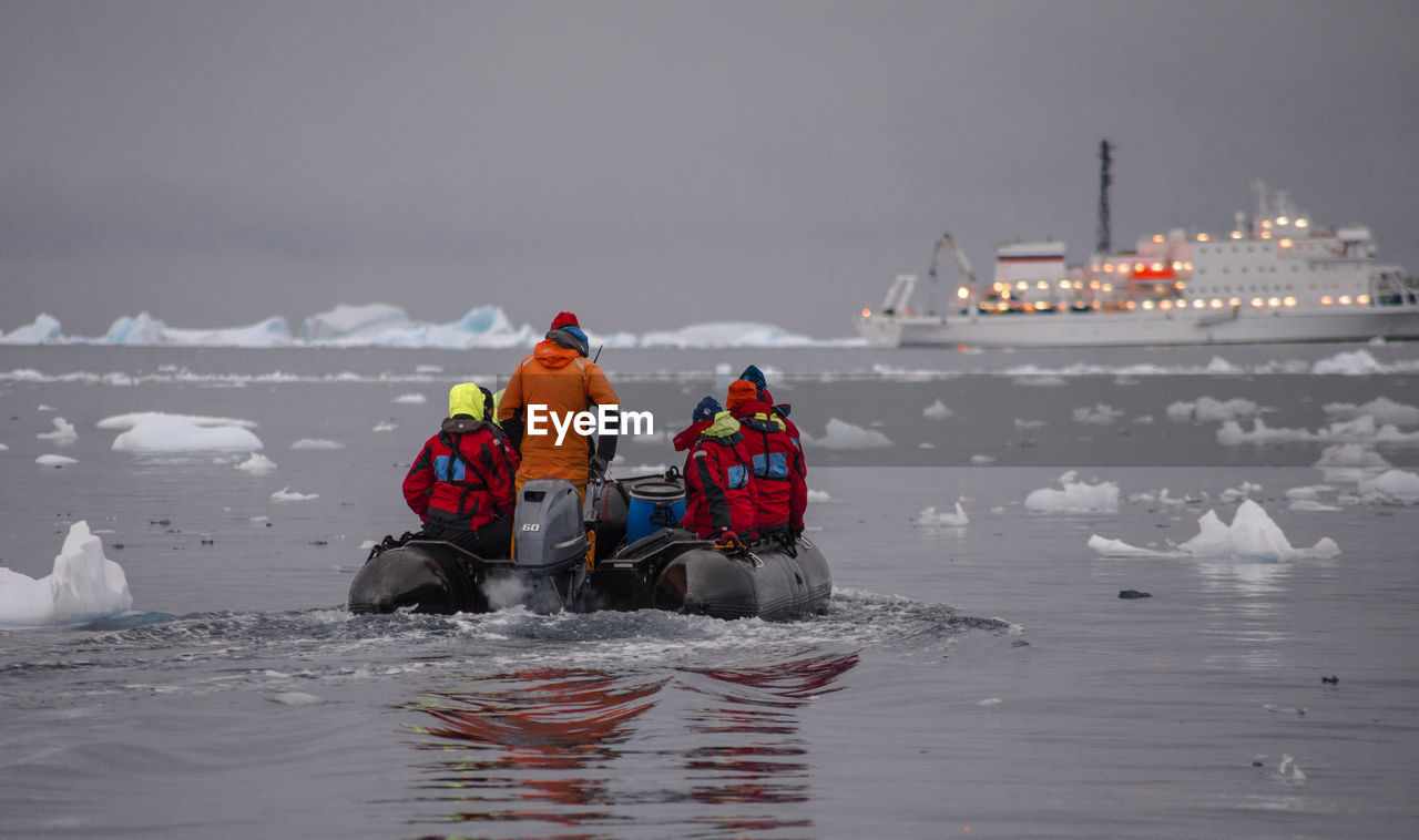 Rear view of people on inflatable raft amidst icebergs in sea during winter