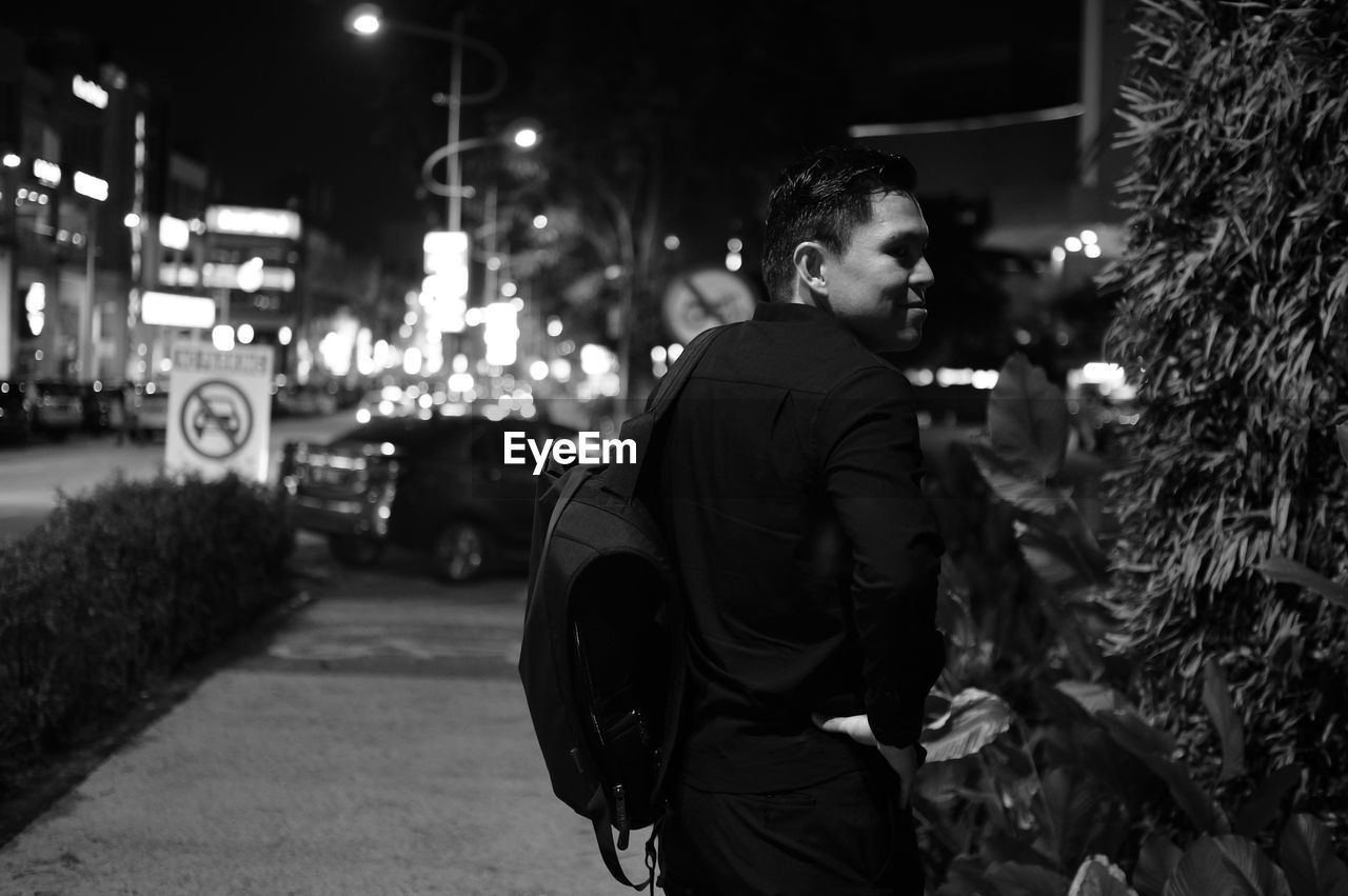 Smiling man looking away by tree in city at night