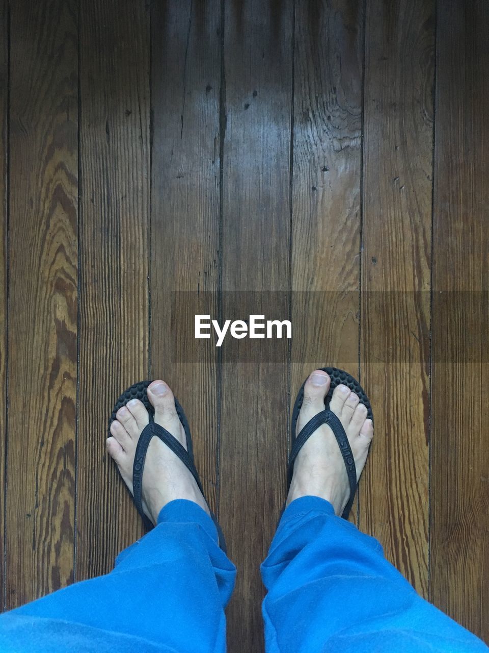 LOW SECTION VIEW OF MAN STANDING ON WOODEN FLOOR