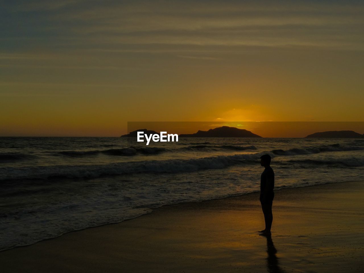 Side view of silhouette man standing on beach against sky during sunset