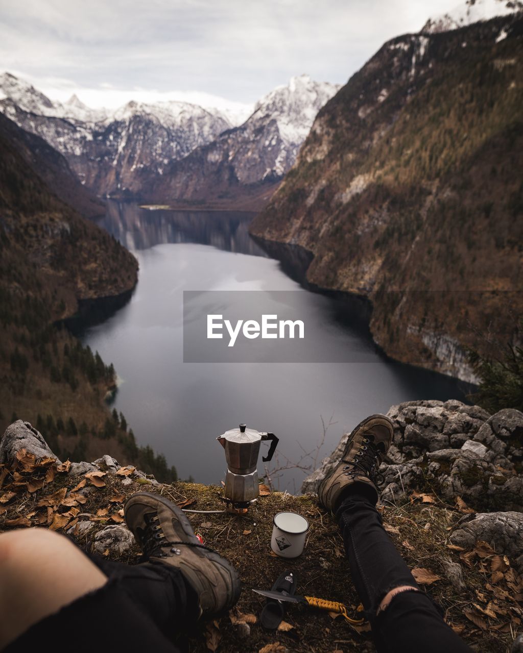 Low section of person sitting on mountain by lake against sky