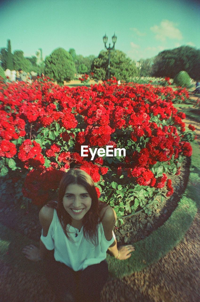 PORTRAIT OF SMILING GIRL WITH RED FLOWERS IN PARK