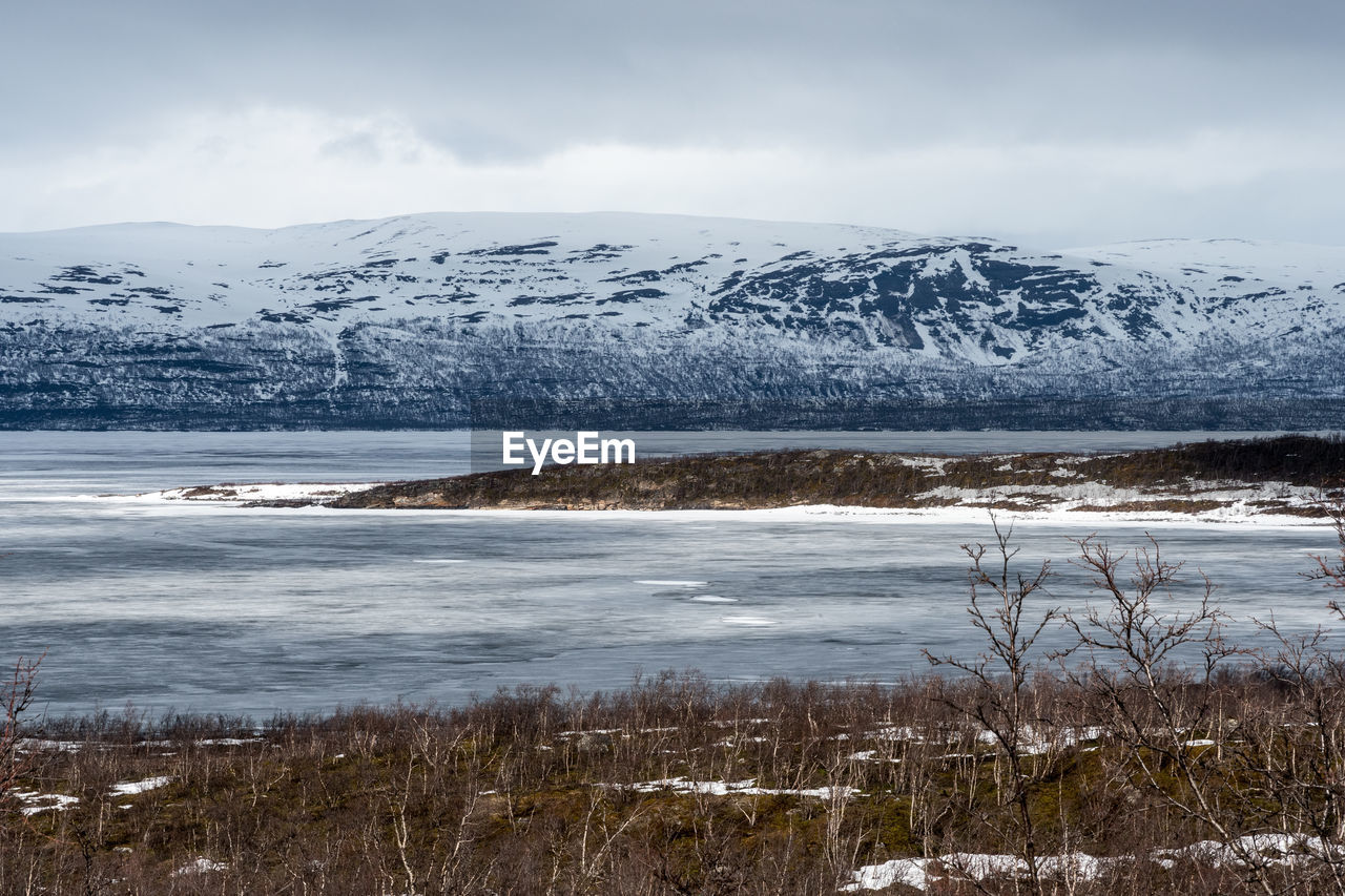 Scenic view of sea by snowcapped mountain against sky