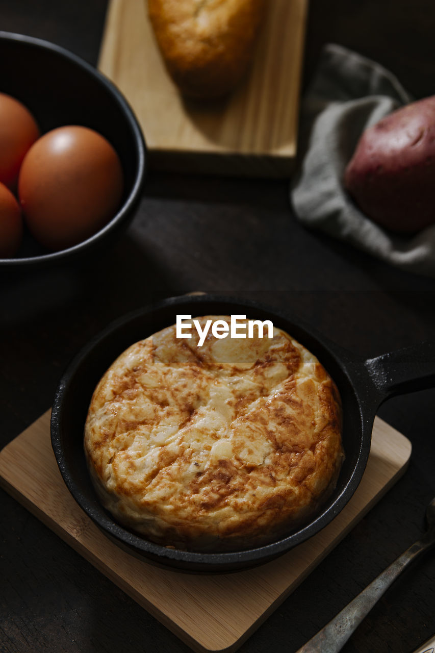 Spanish potato omelette with some fresh eggs shot from high angle over a wooden surface in a dark still life picture. vertical image.