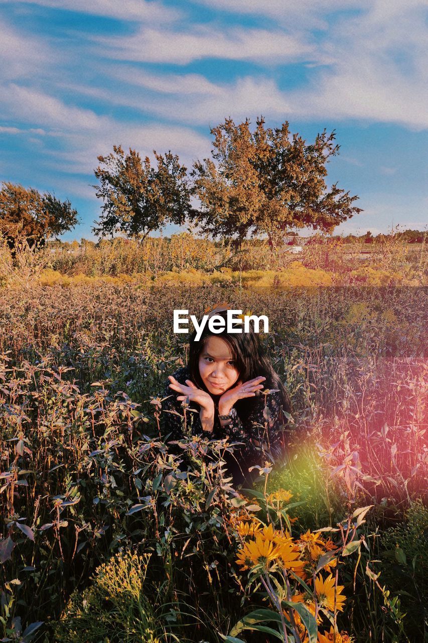 Woman sitting amidst plants on land against sky