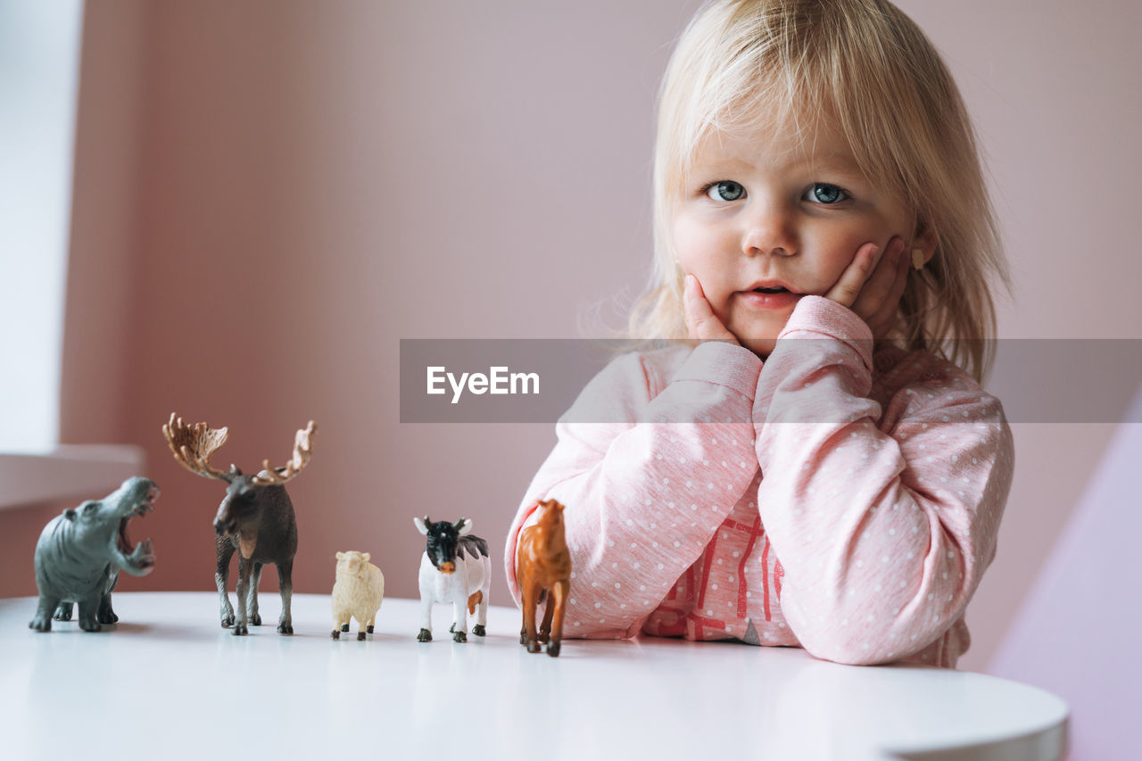 Little girl toddler in pink playing with animal toys on table in children's room at home